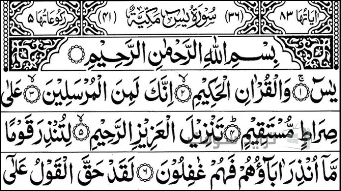 مصحف مفتوح معروض على طاولة خشبية، مع خطوط معقدة وحدود زخرفية مرئية على الصفحات.
